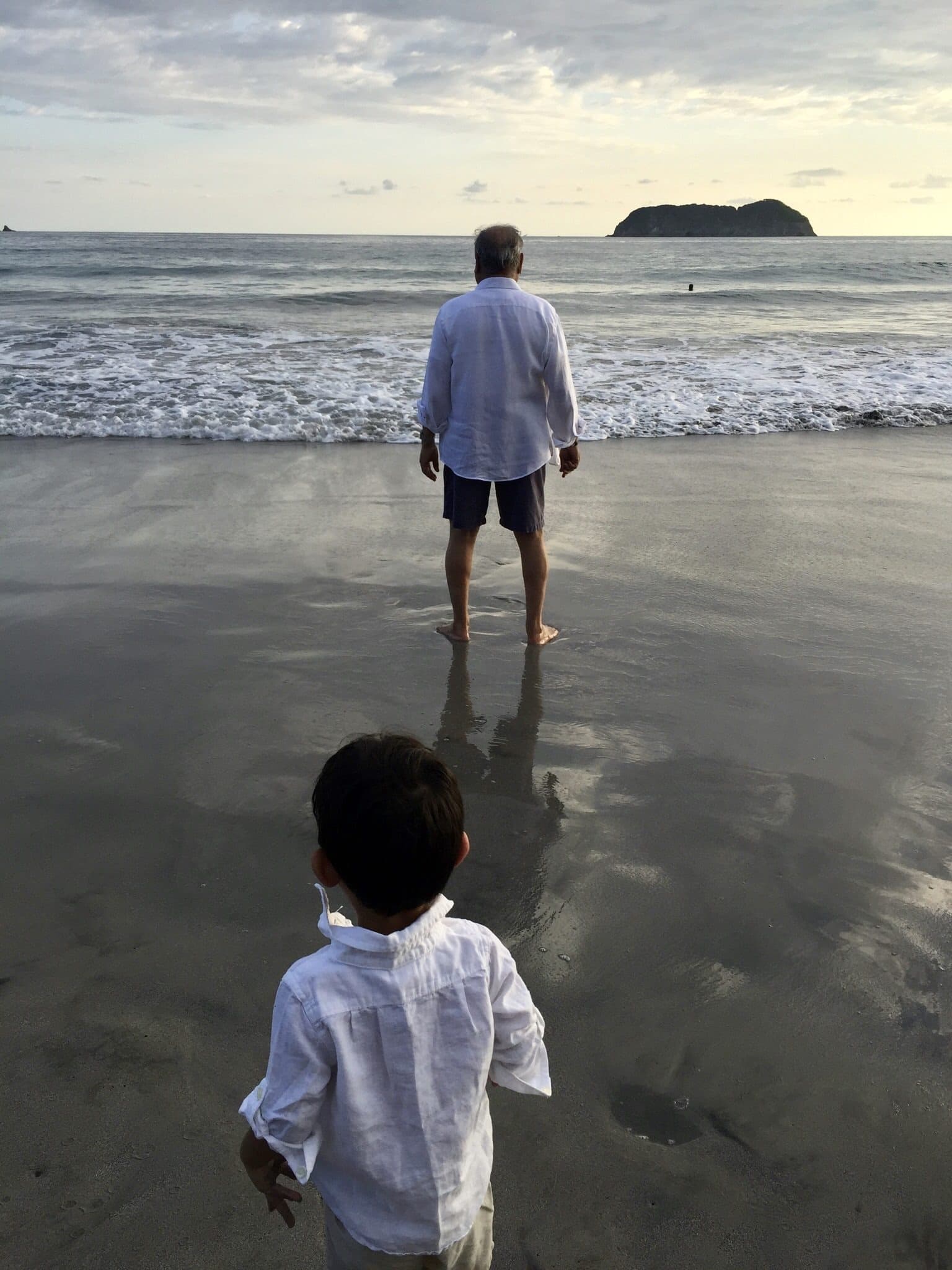 An older man at the water’s edge as a small boy walks toward him